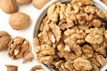 Peeled walnuts in bowl and whole ones on light table, flat lay