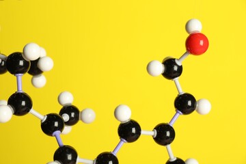 Molecule of retinol (vitamin A) on yellow background, closeup. Chemical model