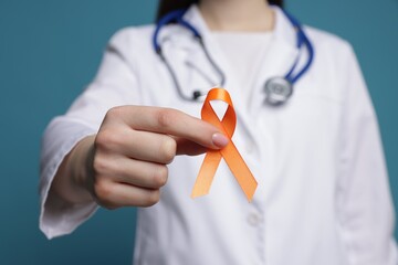 Multiple Sclerosis awareness. Doctor holding orange ribbon on light blue background, closeup