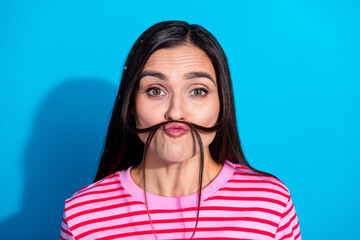Young woman in a striped pink t-shirt making a playful facial expression with hair on a blue...