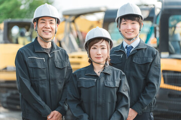 重機の前にいる作業着姿の建設業・建築業の作業員男女
