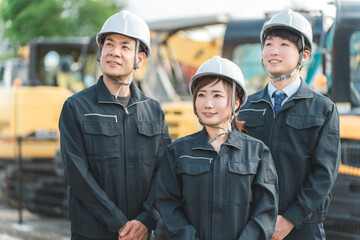 重機の前にいる作業着姿の建設業・建築業の作業員男女
