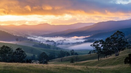 Obraz premium A scenic mountain range bathed in the warm hues of sunset, with mist rising from the valleys.