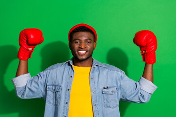 Young man posing confidently in casual fashion with red boxing gloves against vibrant green...