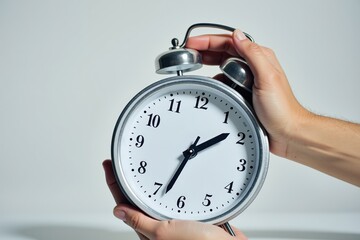 A Close-Up of a Pair of Hands Holding a Classic Silver Alarm Clock at Noon, Emphasizing Time and Its Importance in Daily Life