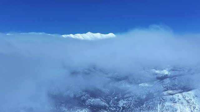 Aerial Mount Nebo Utah winter mountain peak descent. Beautiful late winter Wasatch Mountains. Valley and alpine landscape. Cold weather cloud environment. Rocky ledges, cliffs, canyon and valleys. 