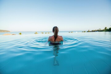 Obraz premium Relaxing Woman in Infinity Pool Overlooking Serene Ocean at Dusk, Capturing Peace and Tranquility of Nature in a Tropical Paradise Setting