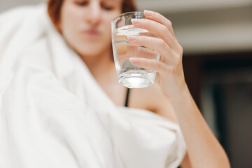 Woman laying in bed with glass of water, white sheet covering head and blanket over body