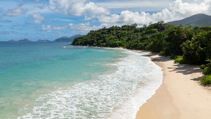 Tropical waves crashing onto a sandy beach, surrounded by dense green vegetation. Anse Louis....