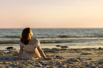 Woman enjoying a serene moment on the beach at sunset with waves and soft sand