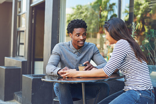 Interracial couple, holding hands and bonding with coffee in city for date, chat or conversation at outdoor cafe. Man, woman or lovers with smile for talk, social discussion or get together in town
