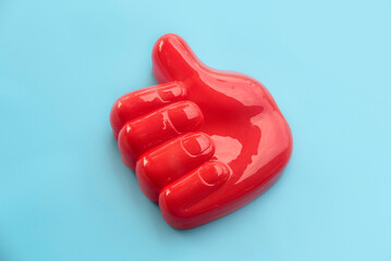Red Thumbs Up Hand Gesture on Light Blue Background.