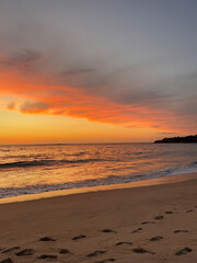 Obraz premium A breathtaking sunset over a serene beach, with vibrant orange and pink hues painting the sky. Gentle ocean waves roll onto the shore, leaving footprints in the golden sand.