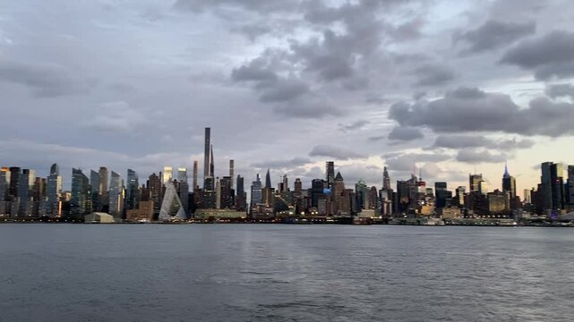 A view of the New York City skyline reflecting the golden hues of sunset over the Hudson River. The modern skyscrapers, including the Empire State Building and Hudson Yards.