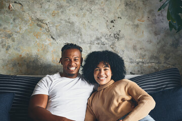Portrait, black couple and relax on sofa at house with love, weekend romance and marriage relationship. Smile, people and partner with embrace for connection, commitment and bonding together of break