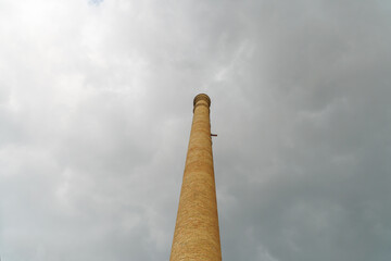 bottom view of a old brick factory chimney with dramatic cloudy sky in background