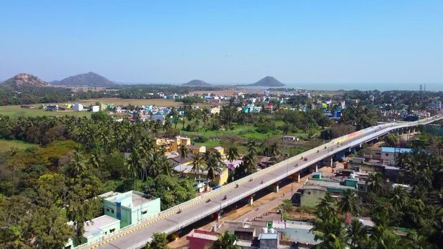 Aerial footage of a flyover bridge passing through a rural village on a clear sunny day