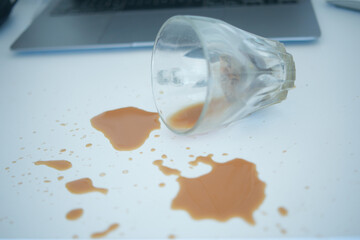 Coffee cup spills on a white table near a laptop at midday