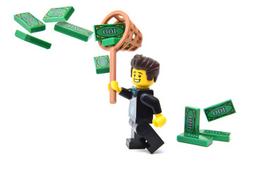 Naklejka premium Lego minifigure of happy male is counting his money green banknotes isolated on white. Editorial illustrative image of finance and banking