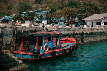 Small red and blue fishing boat with tires as fenders mooring at the pier of a harbor in Southeast Asia