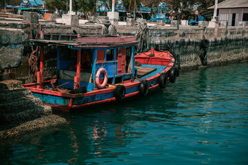 Small colorful wooden fishing boat with tires and lifebuoy mooring in the turquoise water of a harbor in Southeast Asia