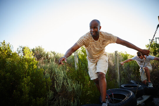 Friends, obstacle and outdoor for balance, exercise and bootcamp tire course for endurance. Men, fitness and workout in nature for athlete, health or masculine strength for tough weekend bonding