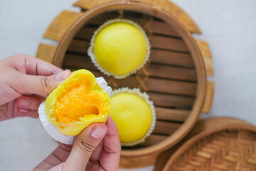 Fluffy Steamed Custard Buns With Bright Yellow And Creamy Golden Lava Filling Served Warm In Bamboo Steamer And Held To Reveal Soft Smooth Texture.