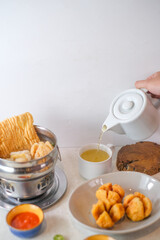 Indonesian Cuanki Soup With Fish Balls, Fried Dumplings, Crispy Crackers, Fresh Lime, Chili Sauces, And Hot Tea Served On A Table For A Hearty Meal.