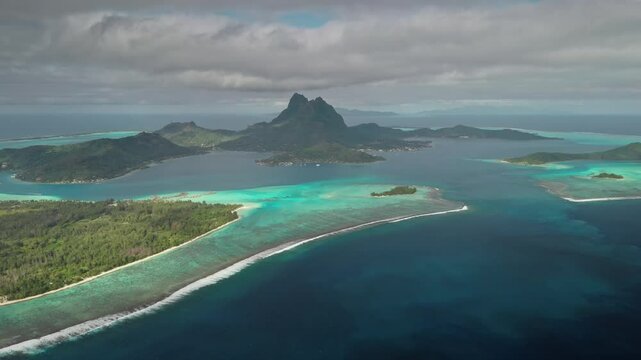 Stunning aerial view of Bora Bora island showing the turquoise lagoon, reef barrier, and lush greenery under a cloudy sky in French Polynesia. Travel tropical vacation concept. Natural background