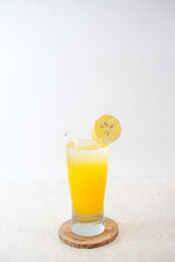 Ice Orange Juice Served In A Tall Glass With Ice Cubes And Orange Slice Garnish, Resting On Wooden Coaster For A Refreshing Drink.