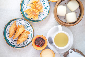 Top View Of Delicious Dim Sum Platter With Fried Dumplings, Steamed Buns In Bamboo Steamer, Green Tea, Cheese Sauce, And Chili Sauce.