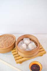 Steamed Hakau Dumplings Served In Bamboo Steamer With Soy Chili Dipping Sauce On Wooden Mat For Asian Culinary Experience Against Light Background.