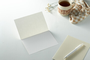 Blank Greeting Card and a Cup of Tea on a White Table With a Cloth and Flowers