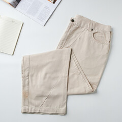 Beige Casual Pants Laid Flat on a White Background With a Notebook and Magazine Nearby