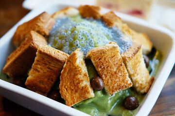 Traditional Korean fresh Bingsu sweet ice dessert with green tea ,toast bread and basil seeds topping on white bowl in cafe