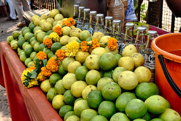 A vibrant market stall displays fresh limes alongside marigold flowers in bright colors, inviting customers to purchase on a sunny day