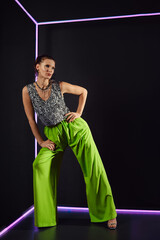 Model poses confidently in vibrant outfit against dark background with neon accents