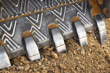Close-up view of an excavator bucket on a gravel ground highlighting metal teeth and textured patterns from heavy use on site
