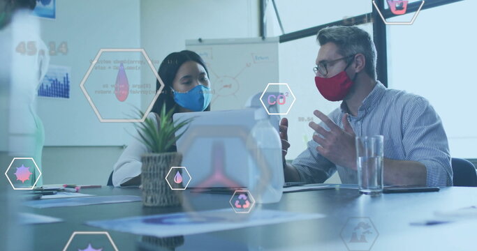 Image of eco icons over diverse business people wearing face masks in office