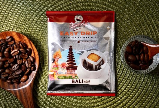 Jakarta, Indonesia - February 20th, 2025 - Kapal Api easy drip bali blend instant coffee sachet isolated on horizontal green place mat background with coffee beans on spoon decor.