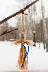 Knot doll with Ukrainian national colours hanging on a tree in winter park. Traditional handcraft...