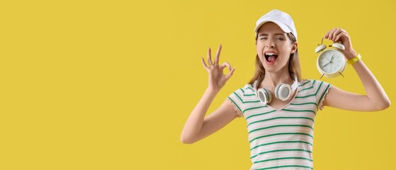 Young woman with alarm clock showing OK on yellow background with space for text
