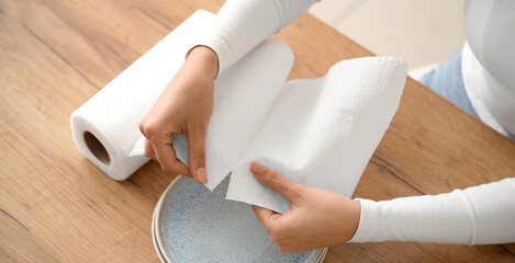 Beautiful young woman with clean plates and roll of paper towels in kitchen, closeup