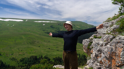 Obraz premium Young man stretching happily on top of mountain in summer against green plateau background
