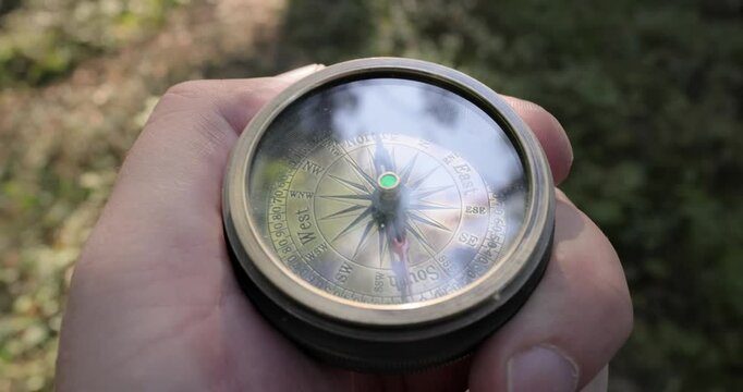 Traveler hand holds a old directional compass in summer forest. Person use compass to find location. Travel concept close-up.