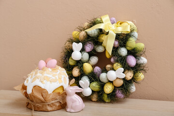 Easter wreath with cake and rabbit on table near beige wall