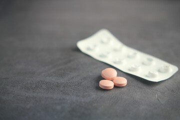 Pink tablets beside an open blister pack on a gray surface