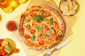 Baking paper with tasty pizza Margarita and plate of potato chips on yellow background