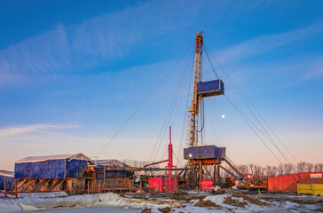 Fototapeta premium Industrial winter landscape featuring an operational drilling rig with support facilities at a remote worksite during daylight hours