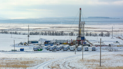 Expansive winter vista of industrial drilling rig complex amid snow-covered plain, featuring crew...